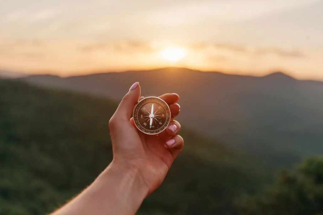 Female hand with compass in summer mountains at sunrise