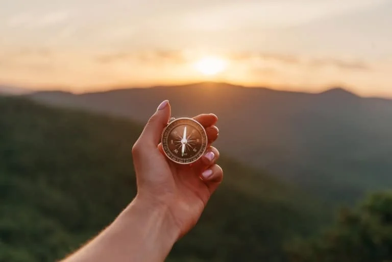 Female hand with compass in summer mountains at sunrise